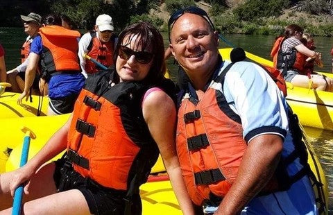 Lesley and her husband Adrian on a rafting trip at the Upper Deschutes River, wearing life jackets and enjoying their time on a raft.